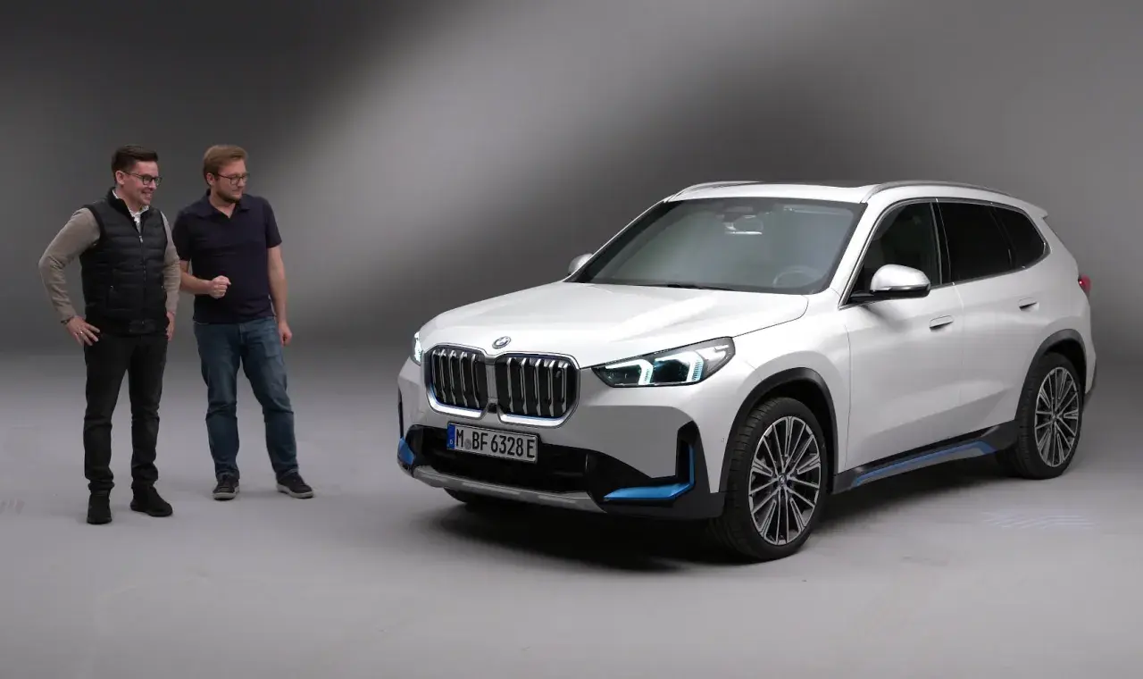 Dwóch mężczyzn obok białego BMW X1 elektryk.