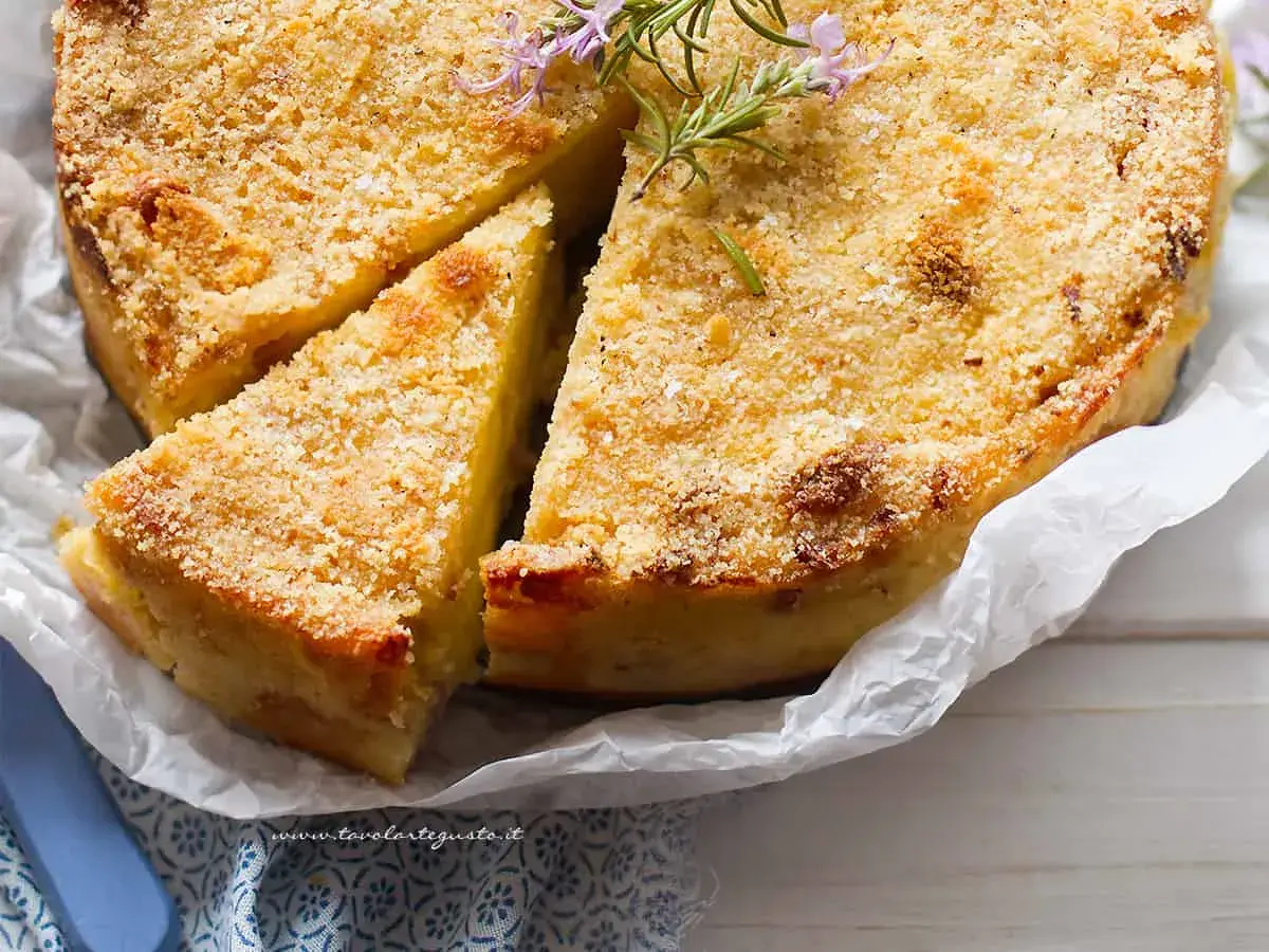 Delizioso gateau di patate dorato e croccante, guarnito con rosmarino fresco. Una fetta è già stata tagliata, invitando ad assaporare questo piatto.