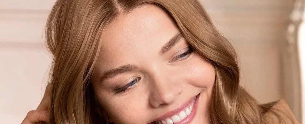 Sonrisa radiante de una mujer con marron ceniza pelo, ojos azules y piel luminosa.