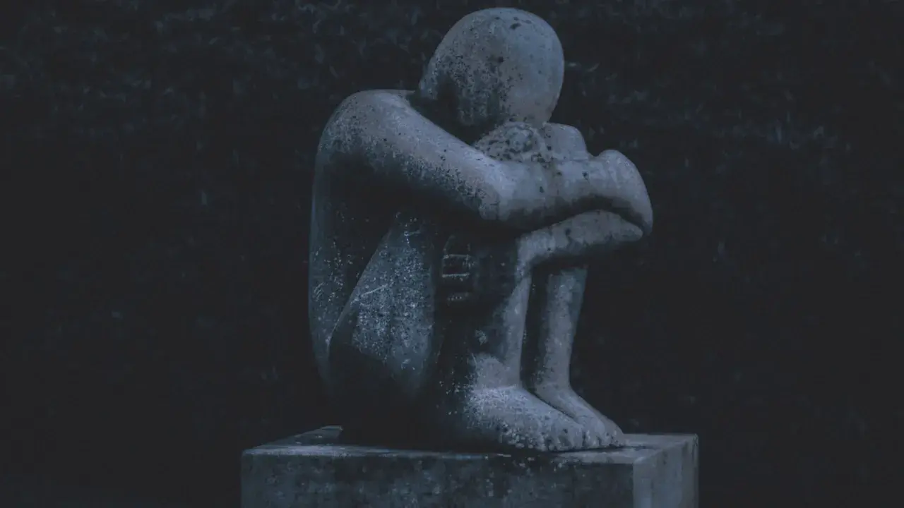 Eine traurige Steinstatue, die sich in sich zusammenkauert, symbolisiert das schlechte Gewissen nach dem Tod des Partners.