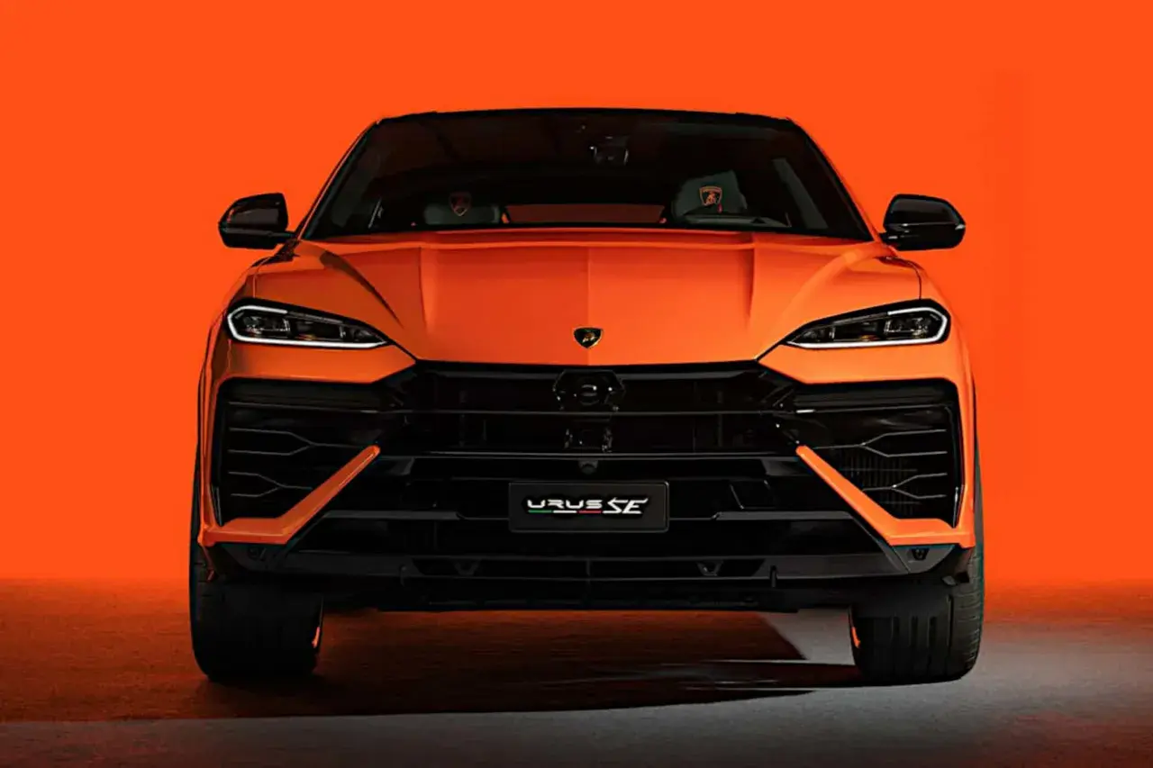 Pomarańczowy Lamborghini Urus SE z przodu, z czarnymi detalami i agresywnym grillem, na tle jaskrawej pomarańczy.