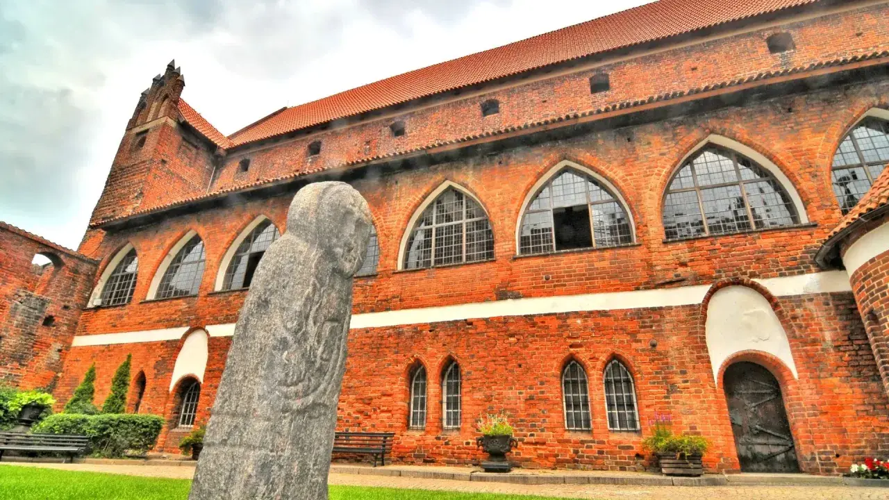 Kamienna postać strzeże murów zamku w Olsztynie. Czerwona cegła i łukowe okna tworzą majestatyczny widok.