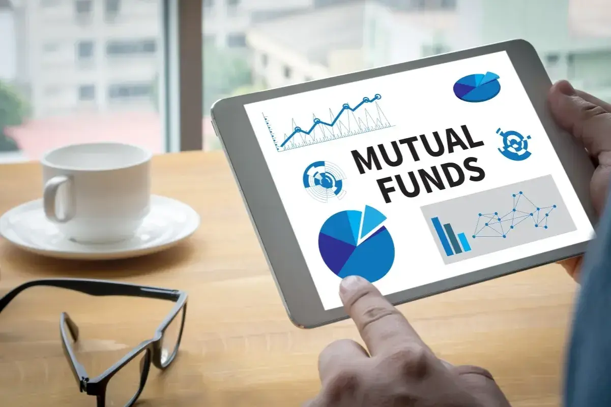 Tablet zeigt "Mutual Funds" mit Diagrammen. Ein Finger tippt auf den Bildschirm, während eine Kaffeetasse und Brille daneben liegen. Der **Ausgabeaufschlag Fonds** wird analysiert.