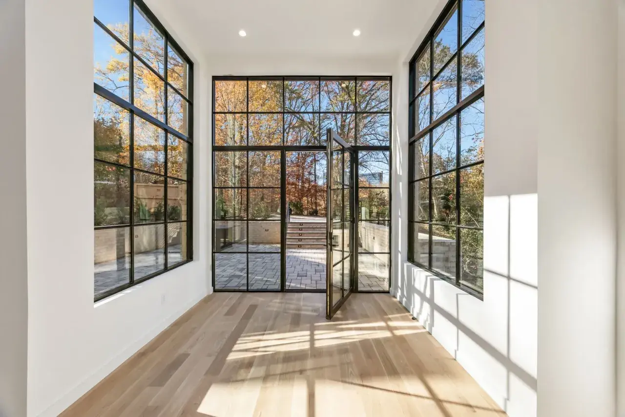 Amplio salón con grandes ventanales de aluminio y madera que dan a un jardín otoñal.