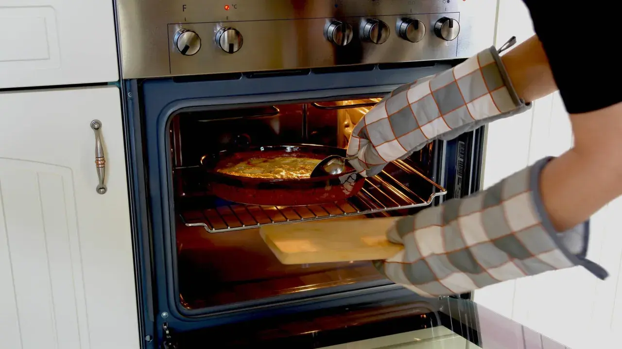 Mit Ofenhandschuhen wird ein Auflauf aus dem Backofen mit Umluft genommen.