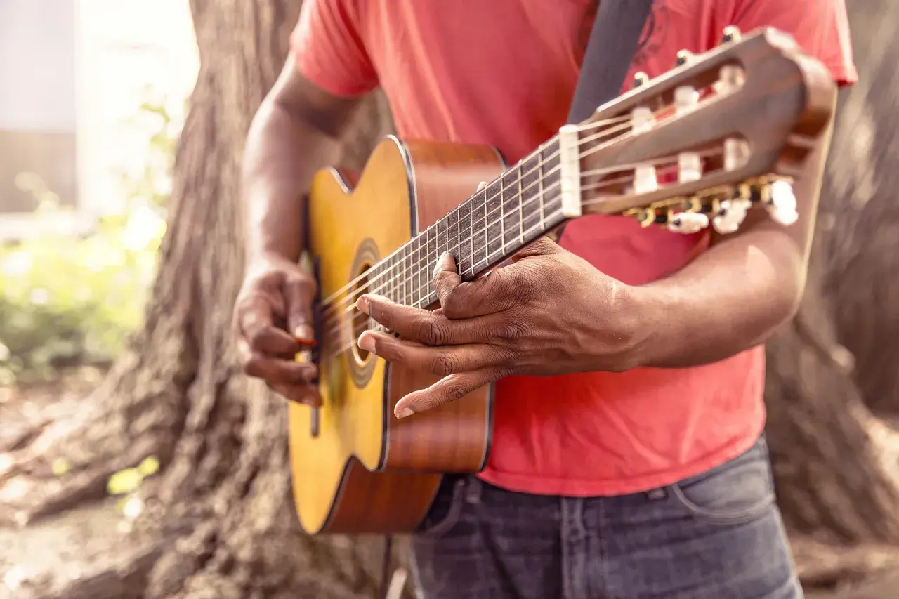 Uomo suona chitarra acustica all'aperto, ideale per imparare canzoni in inglese con testo facile.
