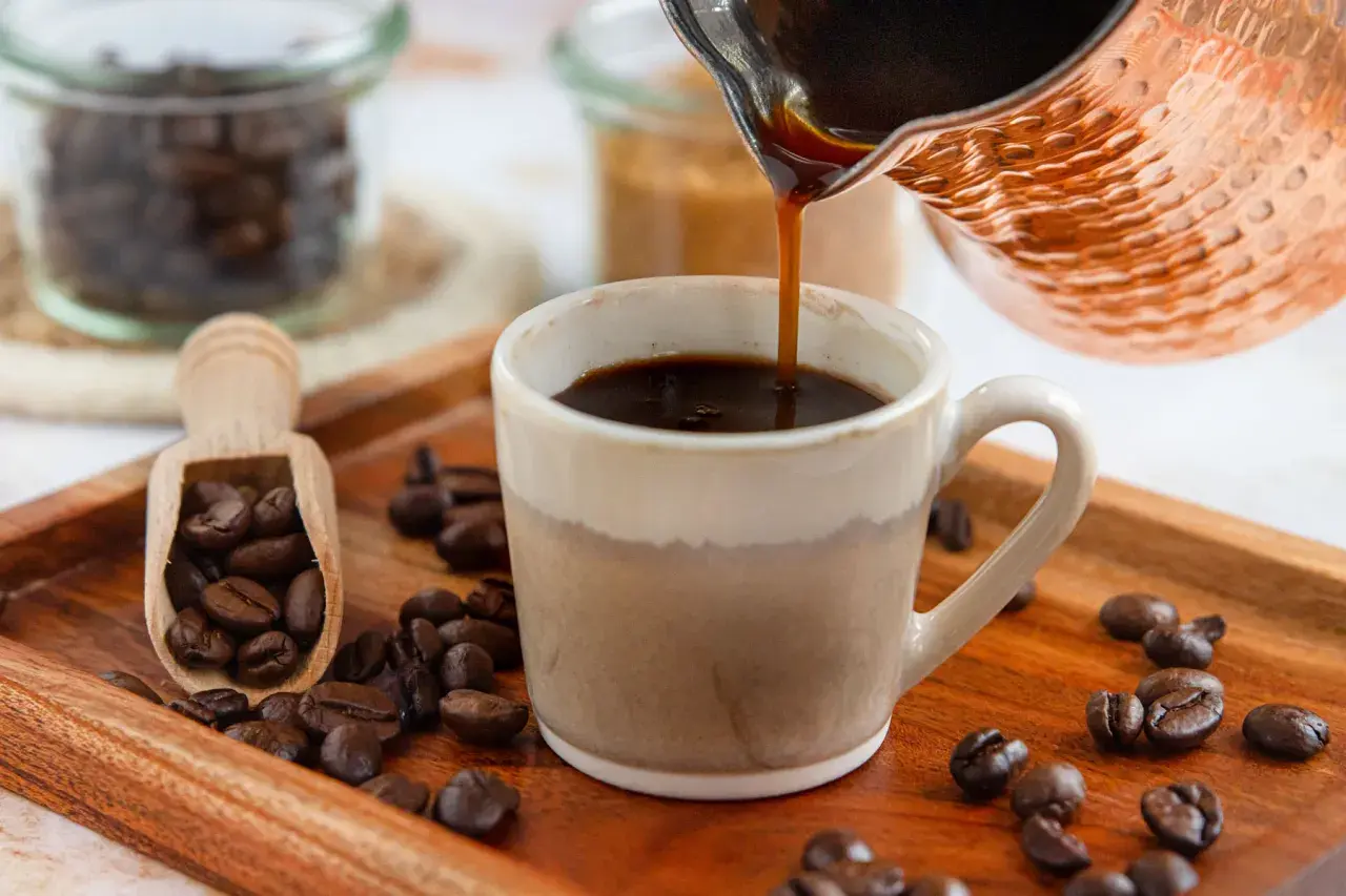 Frisch aufgebrühter türkischer Mokka fließt in eine Tasse. Kaffeebohnen liegen auf einem Holztablett.