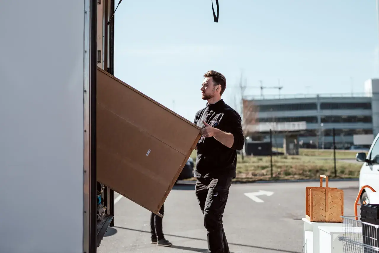 Man packar tavlor för flytt. Han bär en stor, platt kartong mot en lastbil.