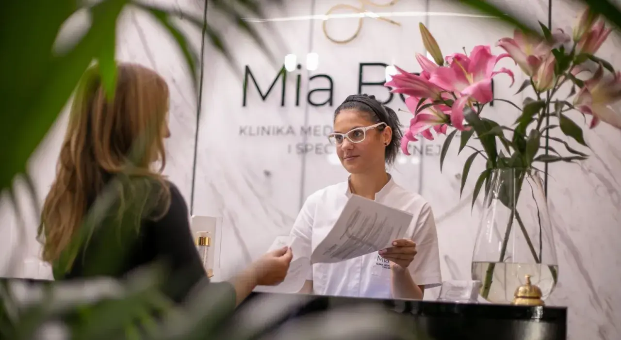 Recepcjonistka w klinice dermatologicznej podaje dokumenty klientce.