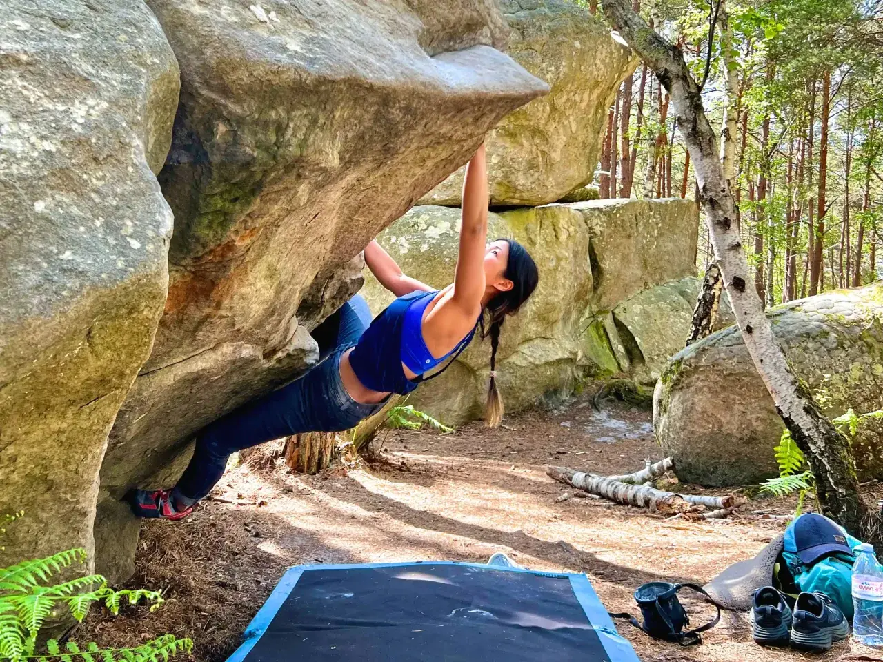 Kobieta wspina się po skale w lesie, doświadczając emocji związanych z boulderingiem w Fontainebleau.