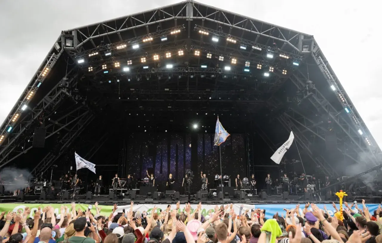 A massive crowd cheers at Glastonbury Festival, a testament to its huge capacity. Performers are on stage under a starry backdrop.