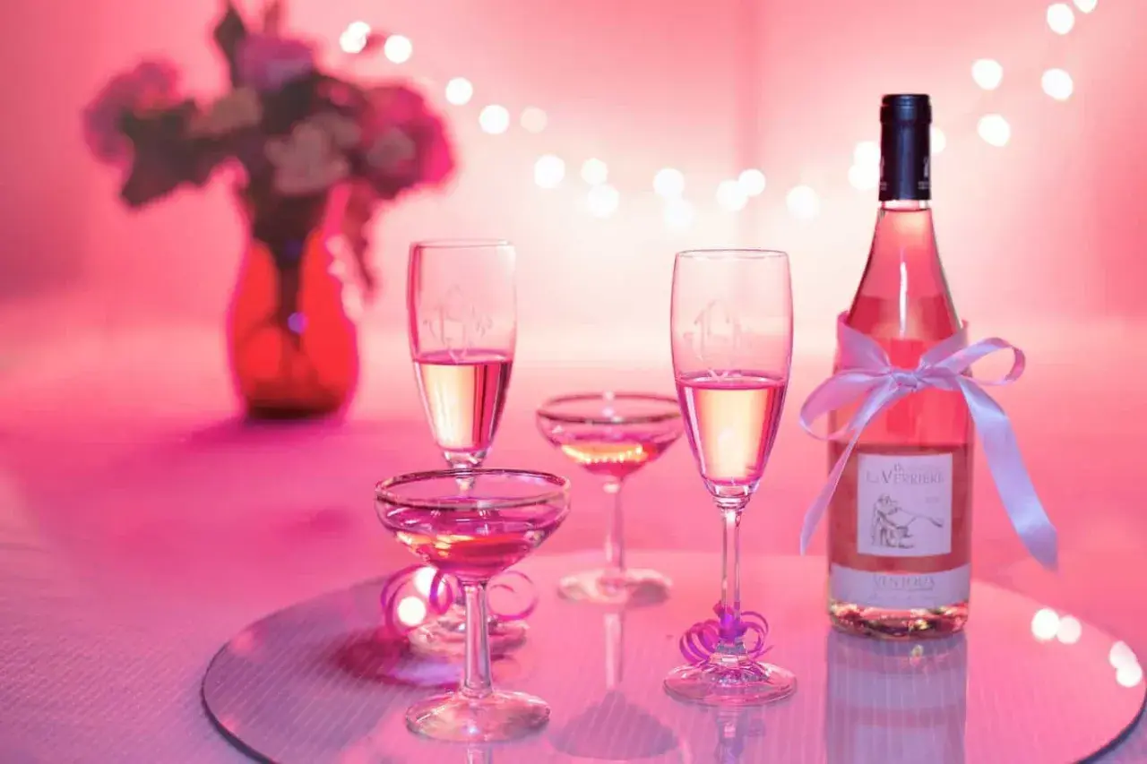 Bottiglia e calici di vino rosato, un brindisi alla vinificazione in rosato, con fiori e luci soffuse.