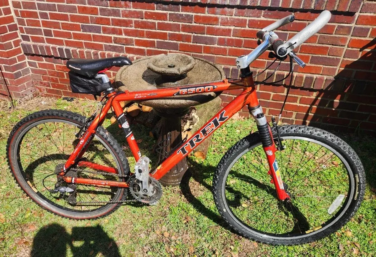 A red Trek 6500 ZX mountain bike rests on grass in front of a brick wall.