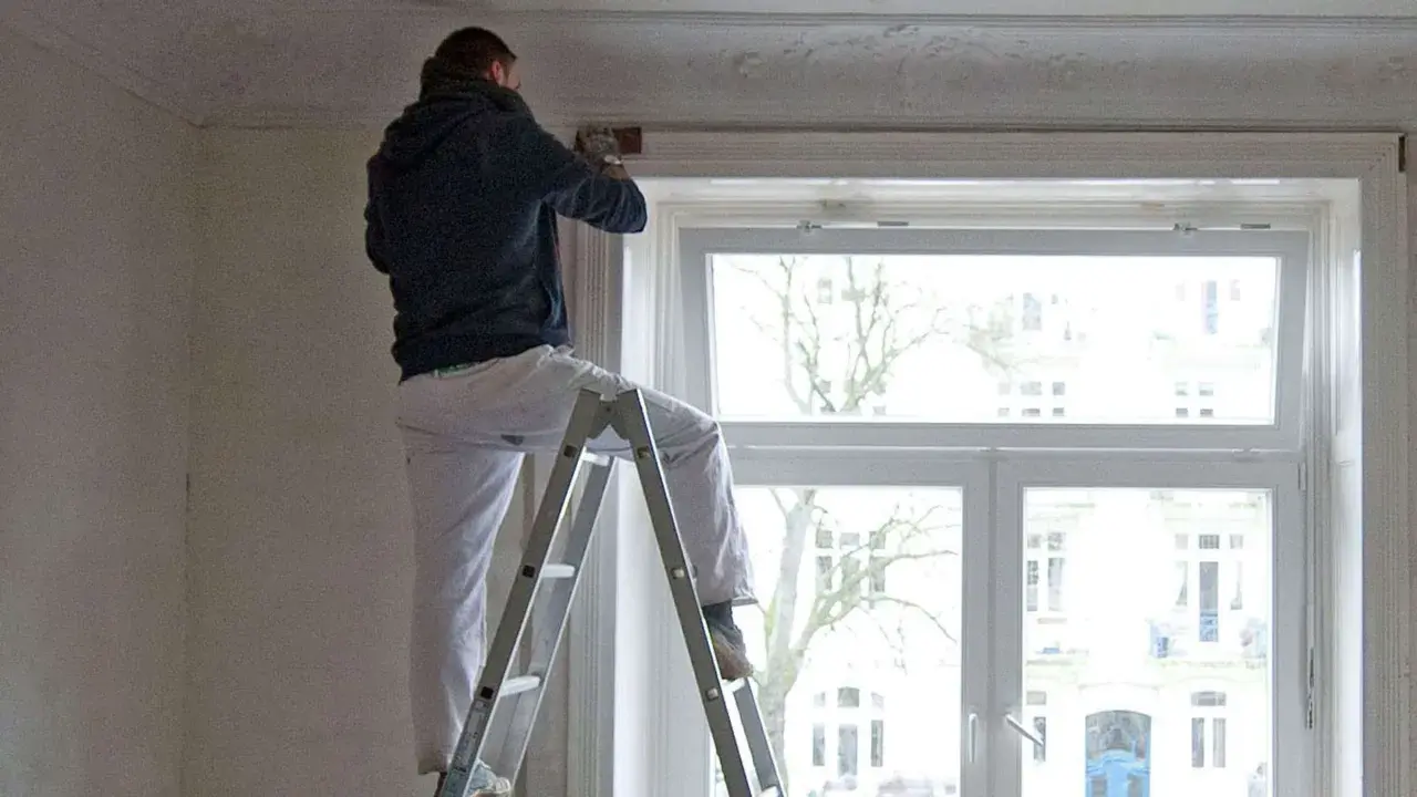Mann auf Leiter renoviert Wohnung. Mieterrechte bei Sanierung beachten.