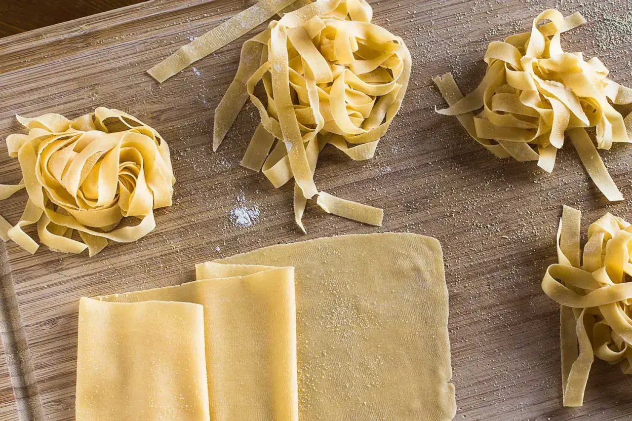 Frischer, selbstgemachter Pastateig, wie im original italienischen Rezept, liegt auf einem Holzbrett. Tagliatelle-Nester und Teigplatten warten auf ihre Zubereitung.
