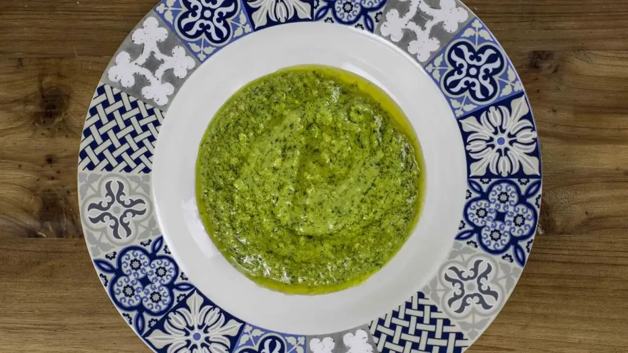 Un plato blanco con un vibrante pesto genovese, adornado con un borde de azulejos azules y grises.
