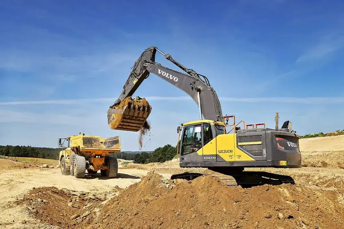 Koparka Volvo wysypuje ziemię do wywrotki. Prace ziemne, ułożenie rur w wykopie cennik bez materiału.