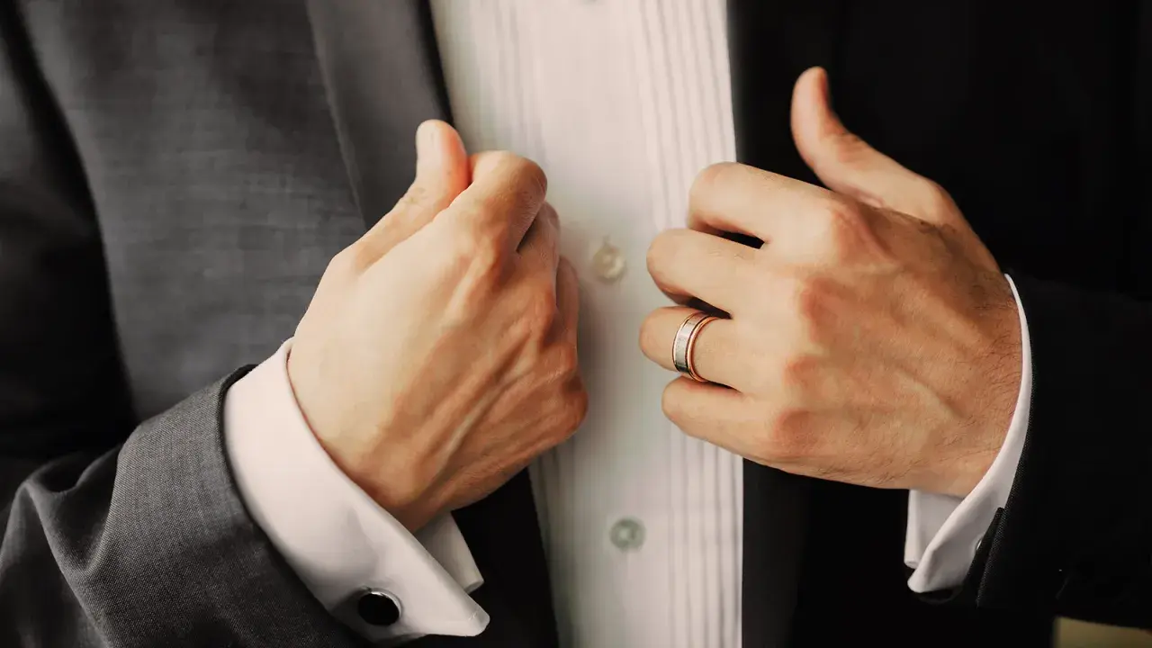 Manos ajustando su traje, mostrando un anillo de bodas. Un detalle elegante para saber donde poner anillos hombre.