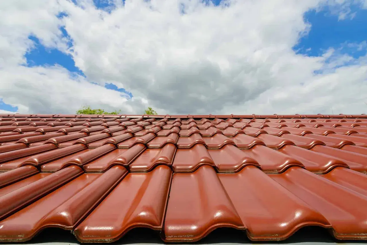 Czerwona dachówka ceramiczna lśni w słońcu. Zastanawiasz się, jaka dachówka ceramiczna najlepsza? Ta prezentuje się okazale.