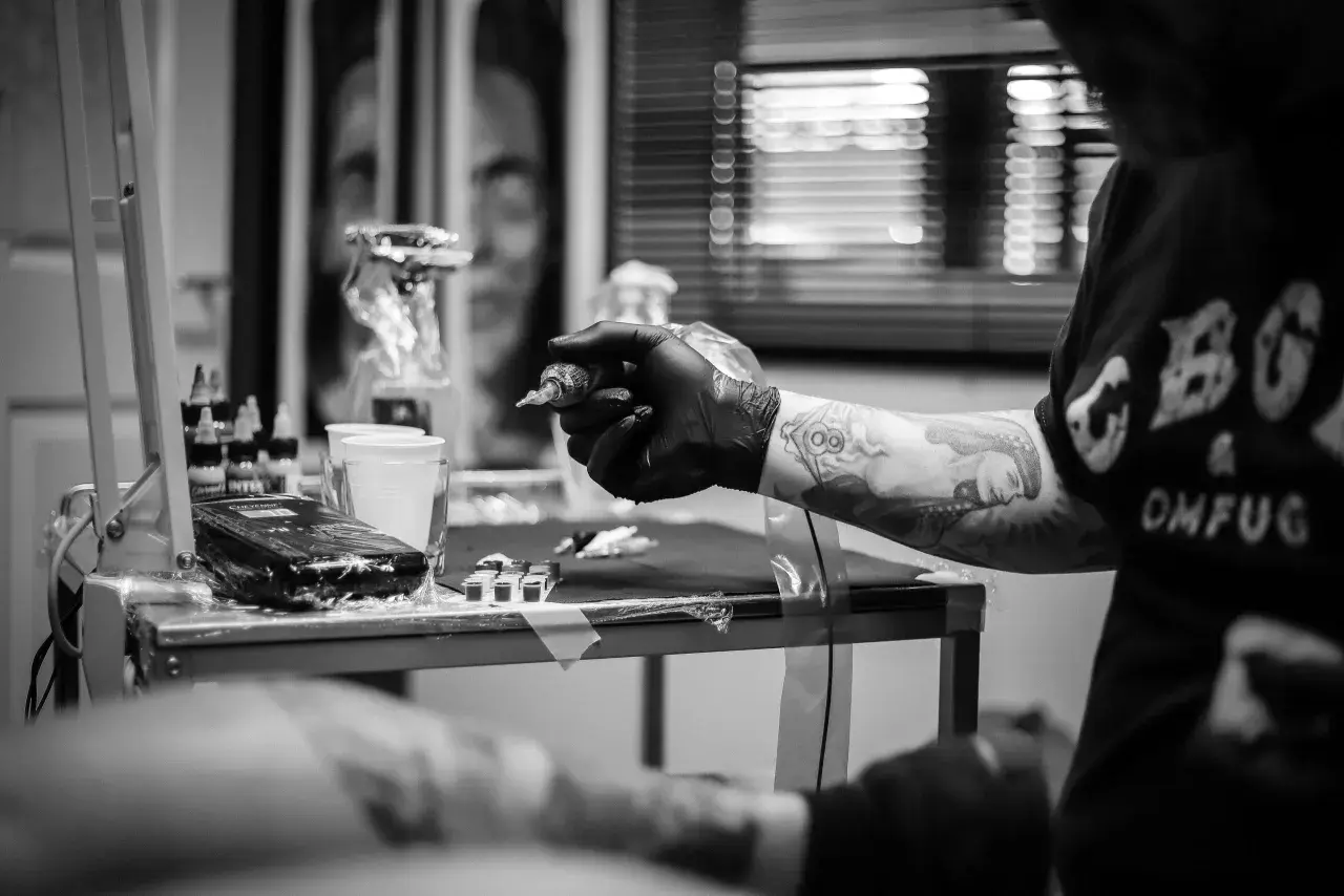Artysta tworzy skomplikowany ornament tattoo na ręce klienta. Widać maszynkę, tusze i przygotowania do sesji.