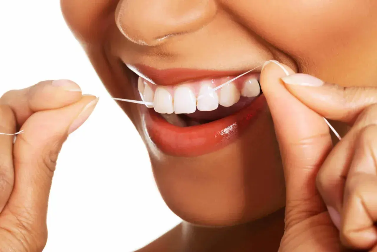 Uśmiechnięta osoba używa nić dentystyczną do czyszczenia zębów. Dbałość o higienę jamy ustnej jest ważna.