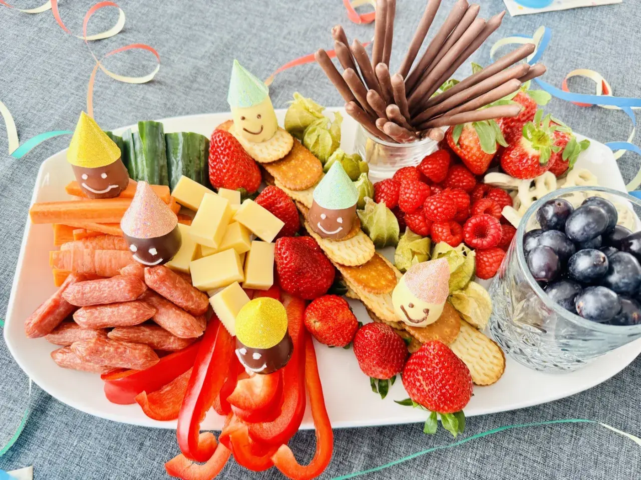 Bunter Snack-Teller mit Früchten, Käse, Würstchen und lustigen Figuren mit Partyhüten – perfekt für Fasching im Kindergarten!