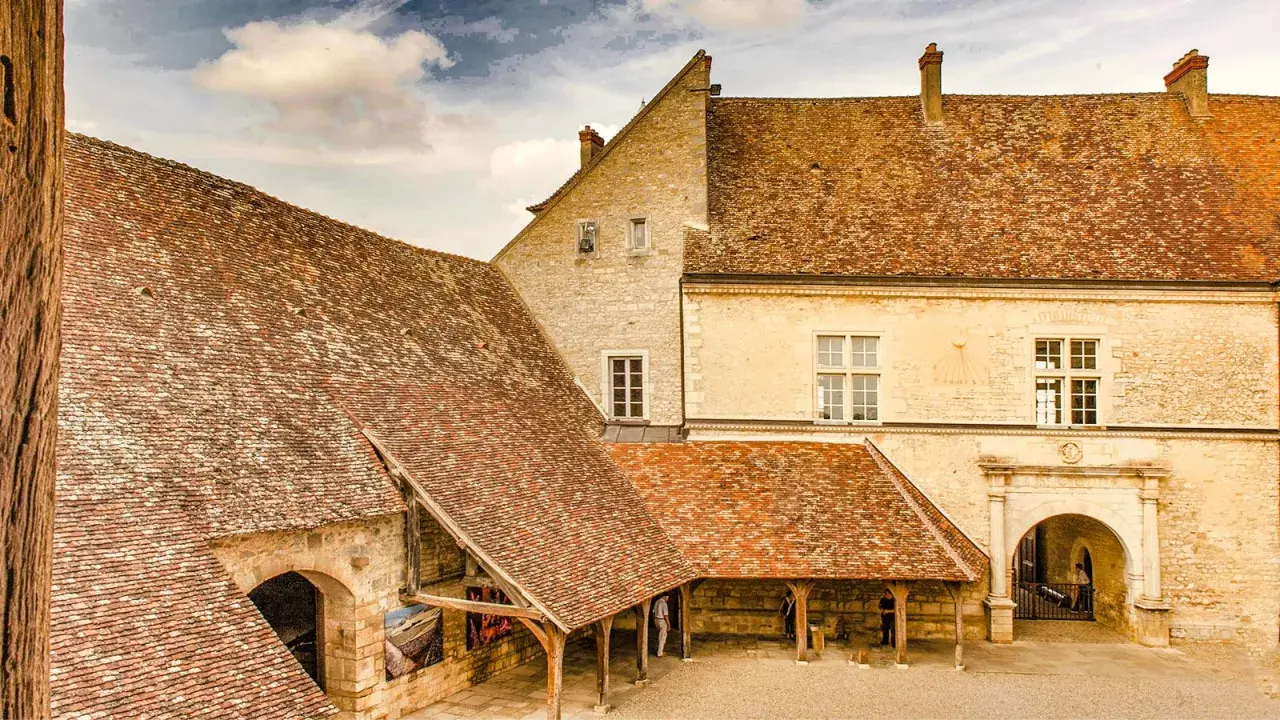 Historisches Gebäude mit Ziegeldächern, ein Torbogen und ein Sonnenuhr. Vielleicht ein Ort, wo man einen exzellenten Chambertin Clos de Bèze genießt.