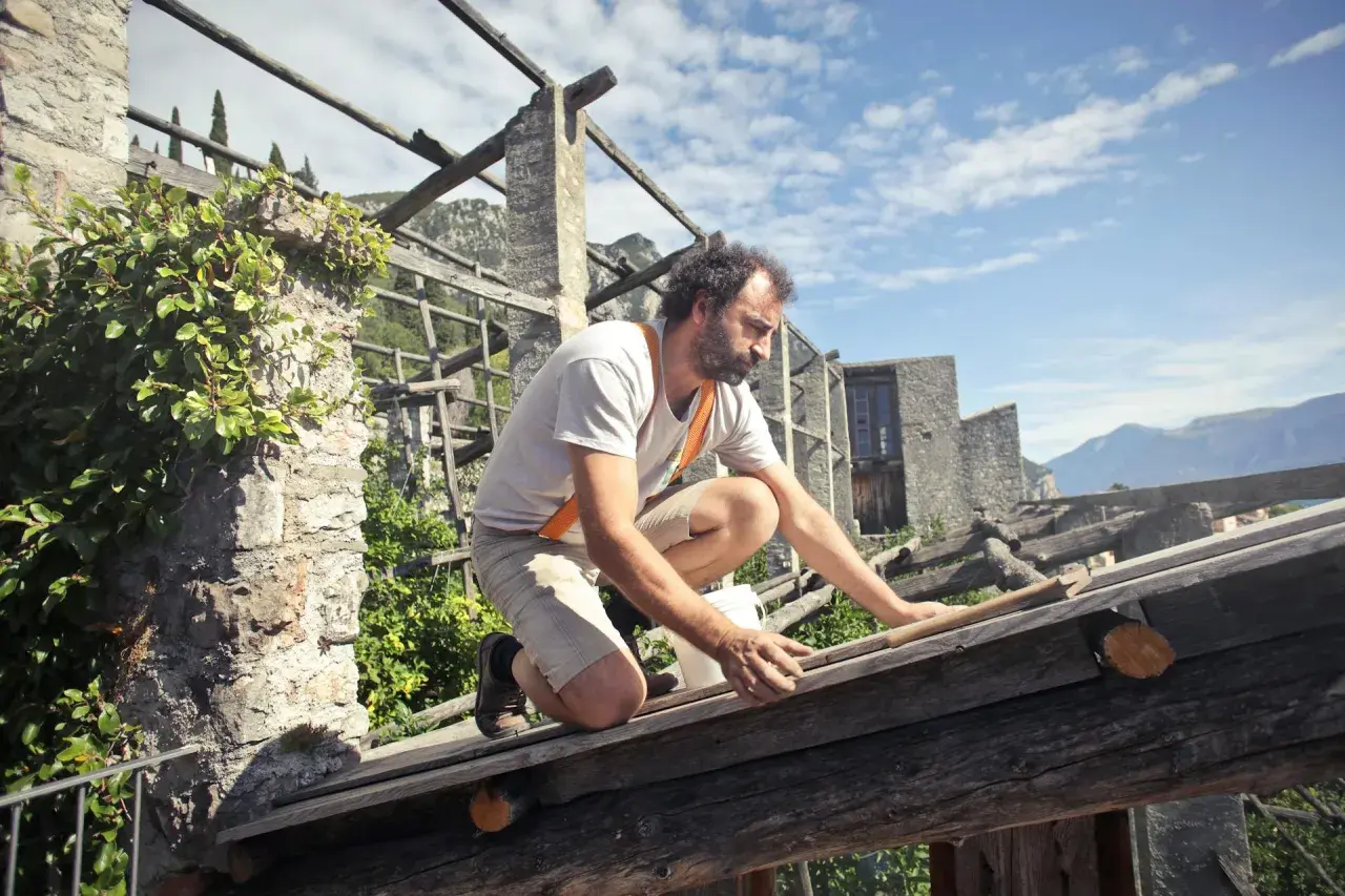 Mężczyzna w ogrodniczkach pracuje na drewnianej konstrukcji dachu.