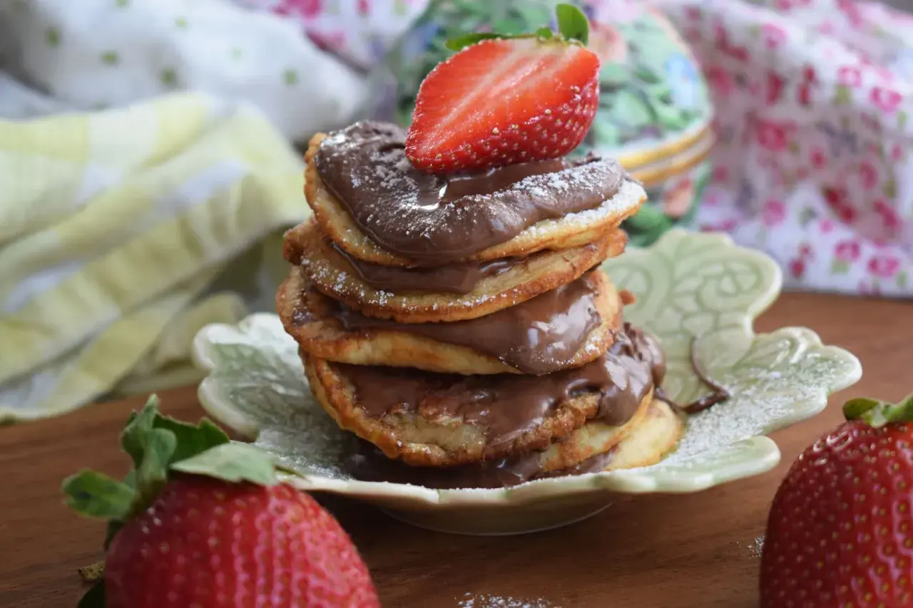 En hög med amerikanska pannkakor med nutella och färska jordgubbar. Pudrad med florsocker.