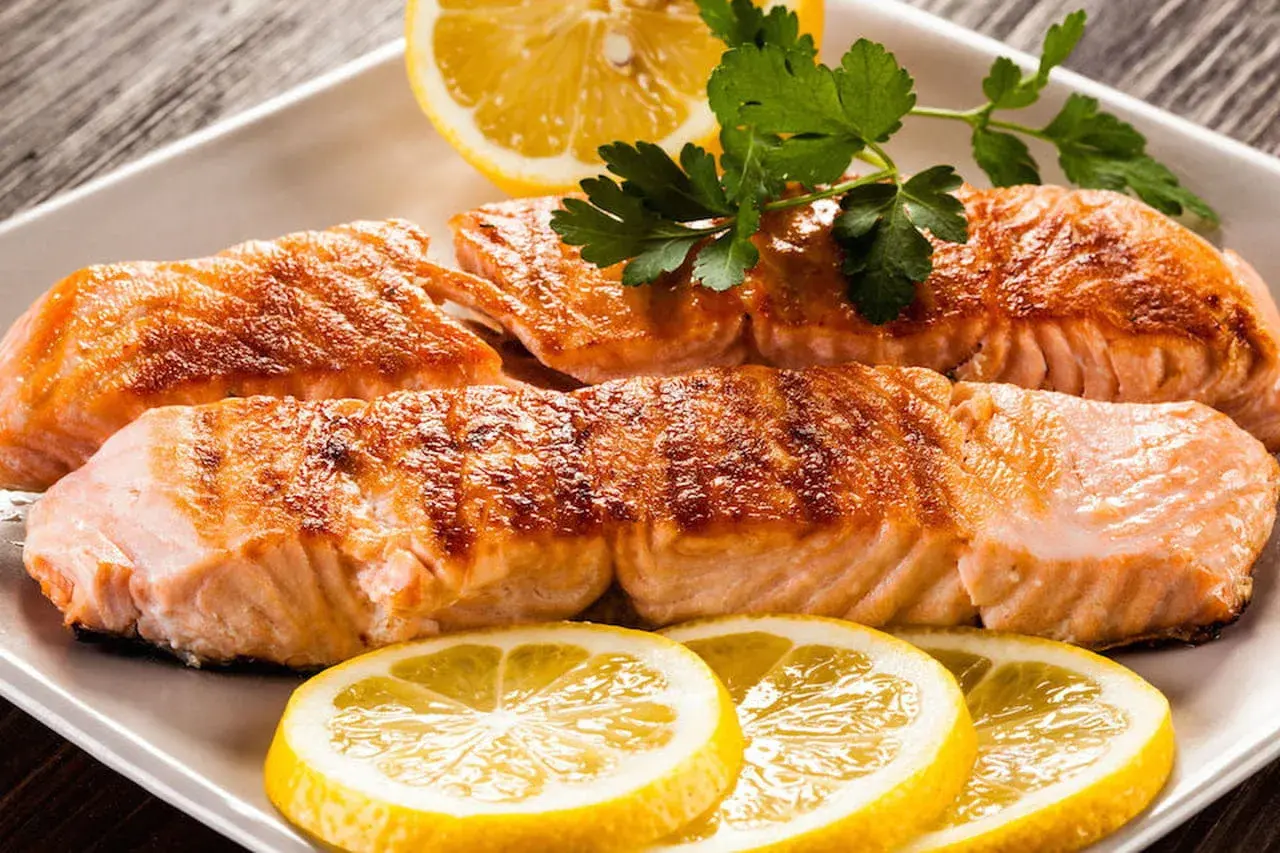 Filetti di salmone succulenti, cotti alla perfezione, con fette di limone e prezzemolo. Un piatto che fa pensare al salmone in gravidanza, ricco di omega-3.