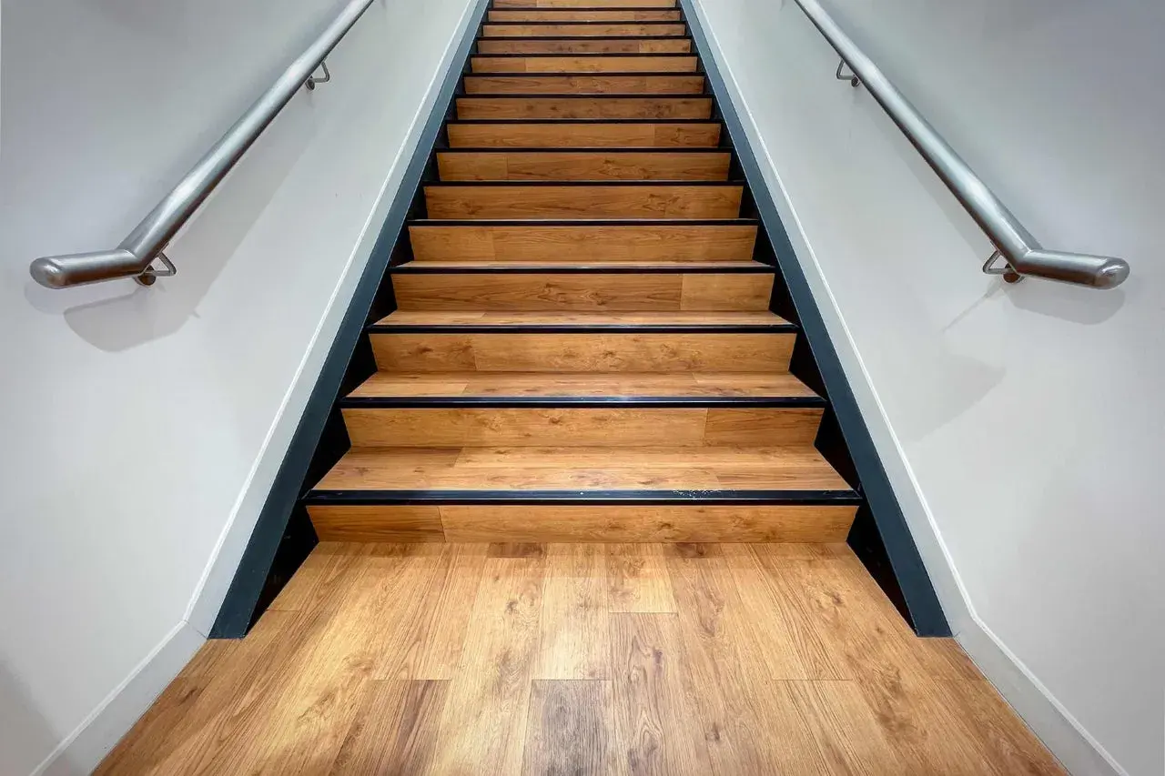 Moderne Treppe mit Holzoptik-Belag. Die Betonstufen sind professionell verkleidet, mit schwarzer Kante und Edelstahl-Handlauf.