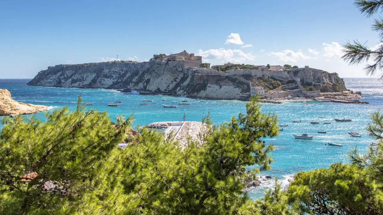 Vista panoramica del paese delle Isole Tremiti, con case bianche arroccate su scogliere a picco sul mare turchese, punteggiato da barche.