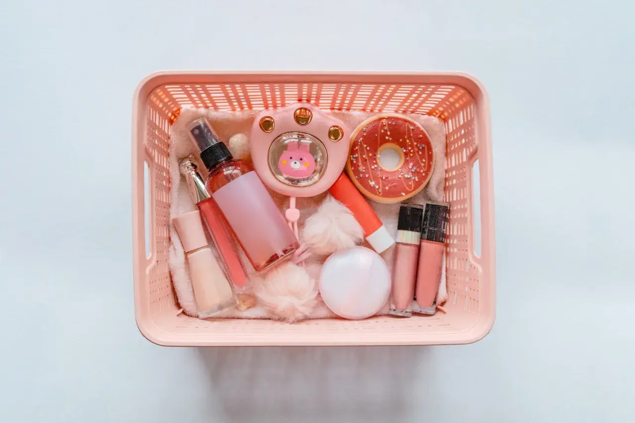 Rosa korg med smink på flyget: läppglans, puder, parfymflaska och en söt liten fläkt.