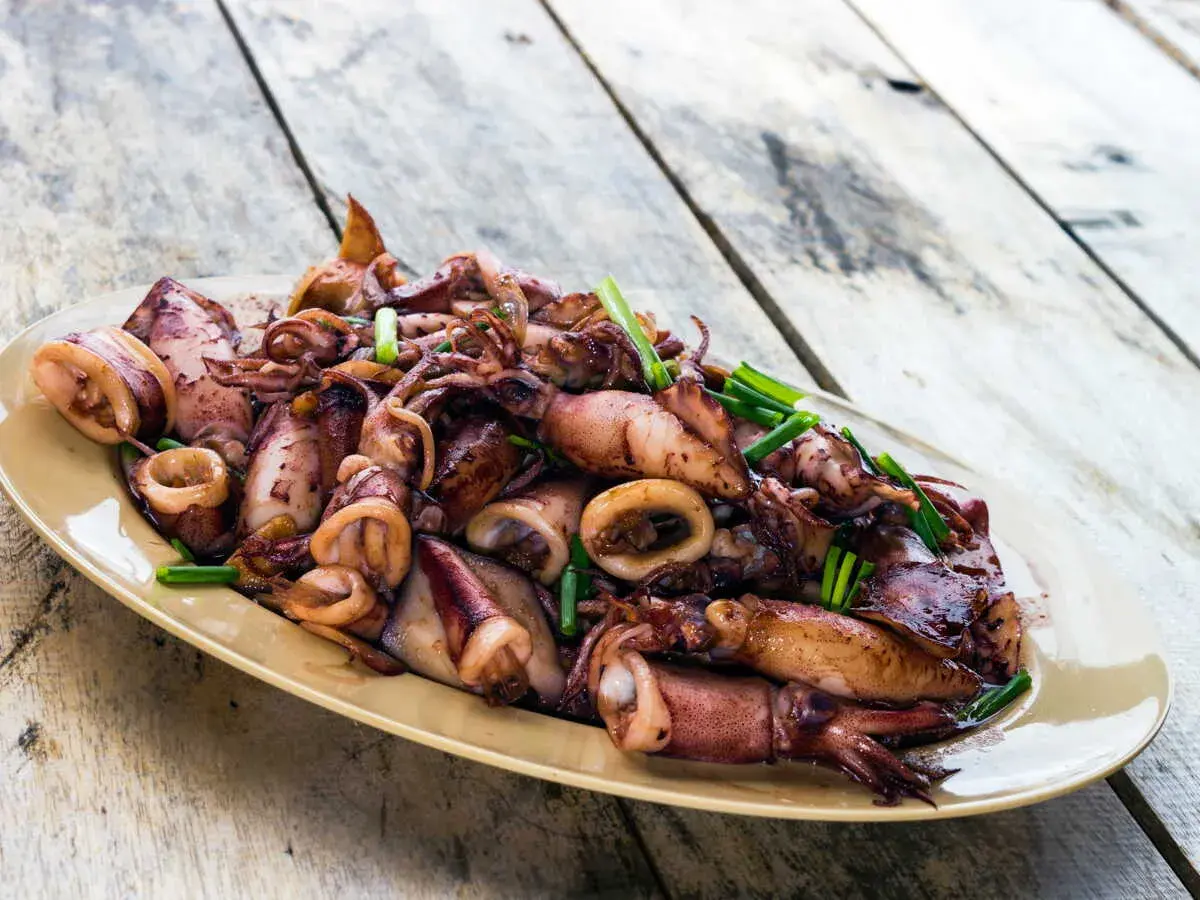 Assiette d'encornets sautés, une délicieuse recette encornet, garnie de ciboule fraîche sur une table en bois.