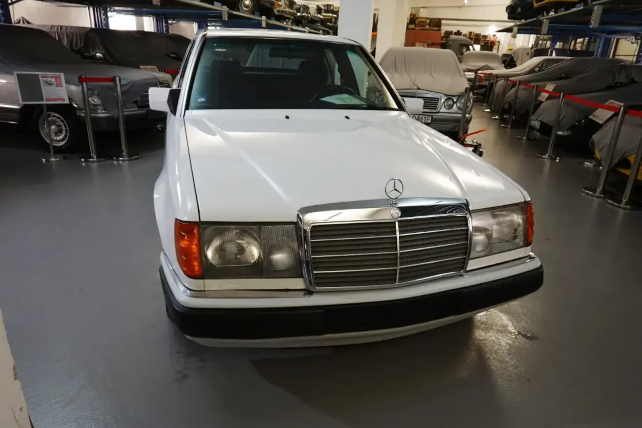 Biały Mercedes "Baleron" z lat 80. stoi w muzeum obok innych zakrytych samochodów.