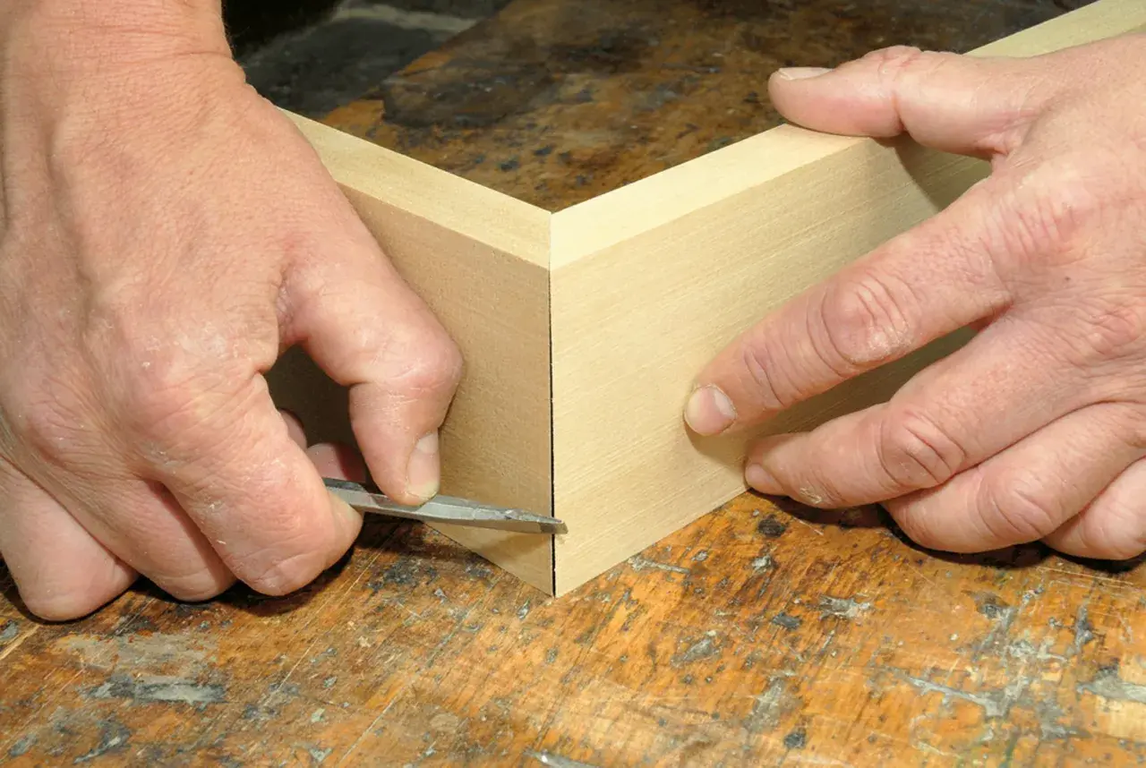 Präzises Gehrung schneiden: Hände führen ein scharfes Werkzeug an Holzleisten entlang, um eine perfekte Ecke zu schaffen. Ein kleiner Trick für saubere Verbindungen.