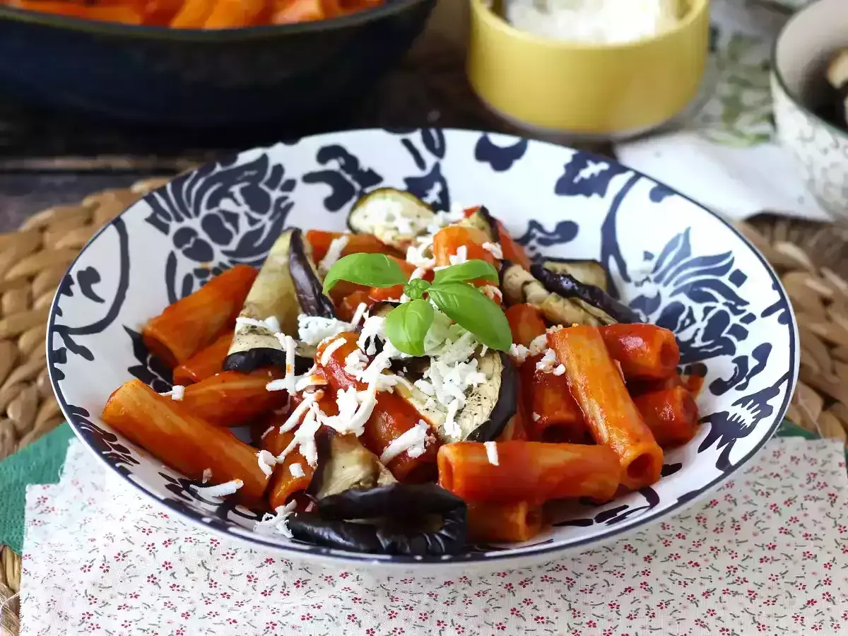 En skål med pasta alla norma med aubergine, tomatsås och basilika, toppad med riven ost.