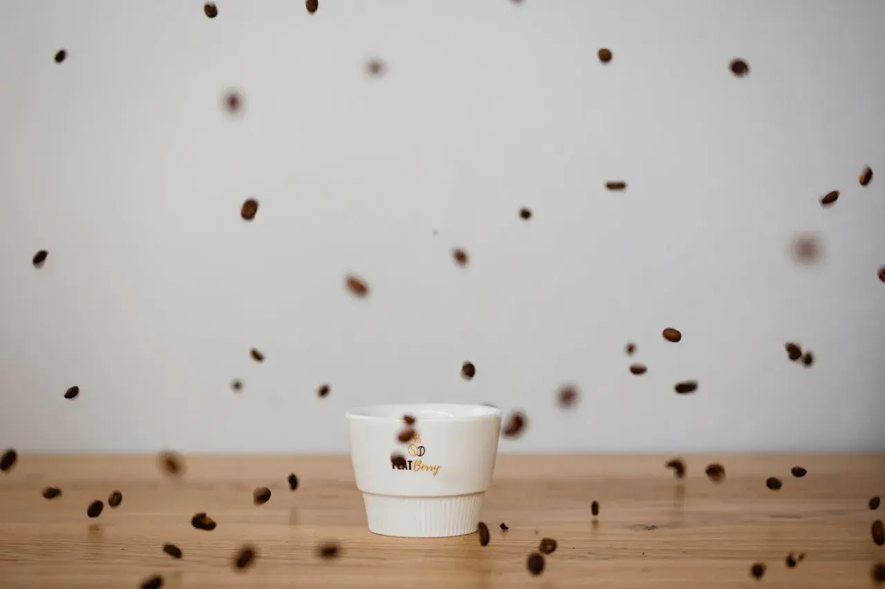 Kaffeebohnen tanzen um eine weiße Tasse. Der Duft verspricht vollen Kaffee Geschmack.