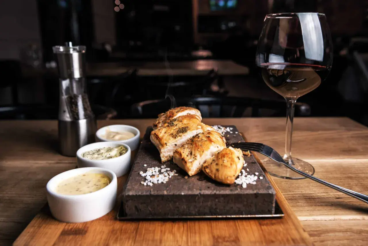 Un plat de poulet grillé avec trois sauces, du sel, un moulin à poivre et un verre de vin rouge. La question est : quel vin avec viande blanche ?