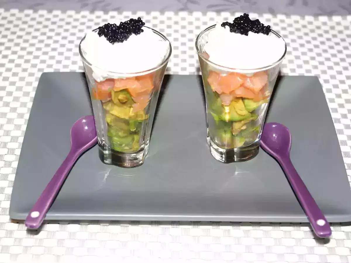 Deux verrines avocat saumon, garnies de crème et de caviar, prêtes à être dégustées avec leurs cuillères violettes.