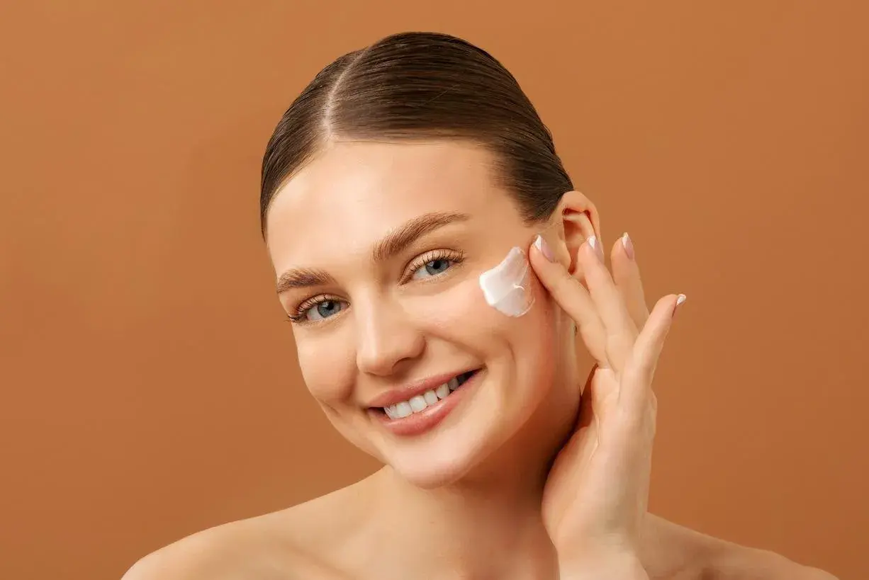 Mujer sonriente aplicándose crema facial. Una rutina de belleza con retinol y vitamina c para una piel radiante.