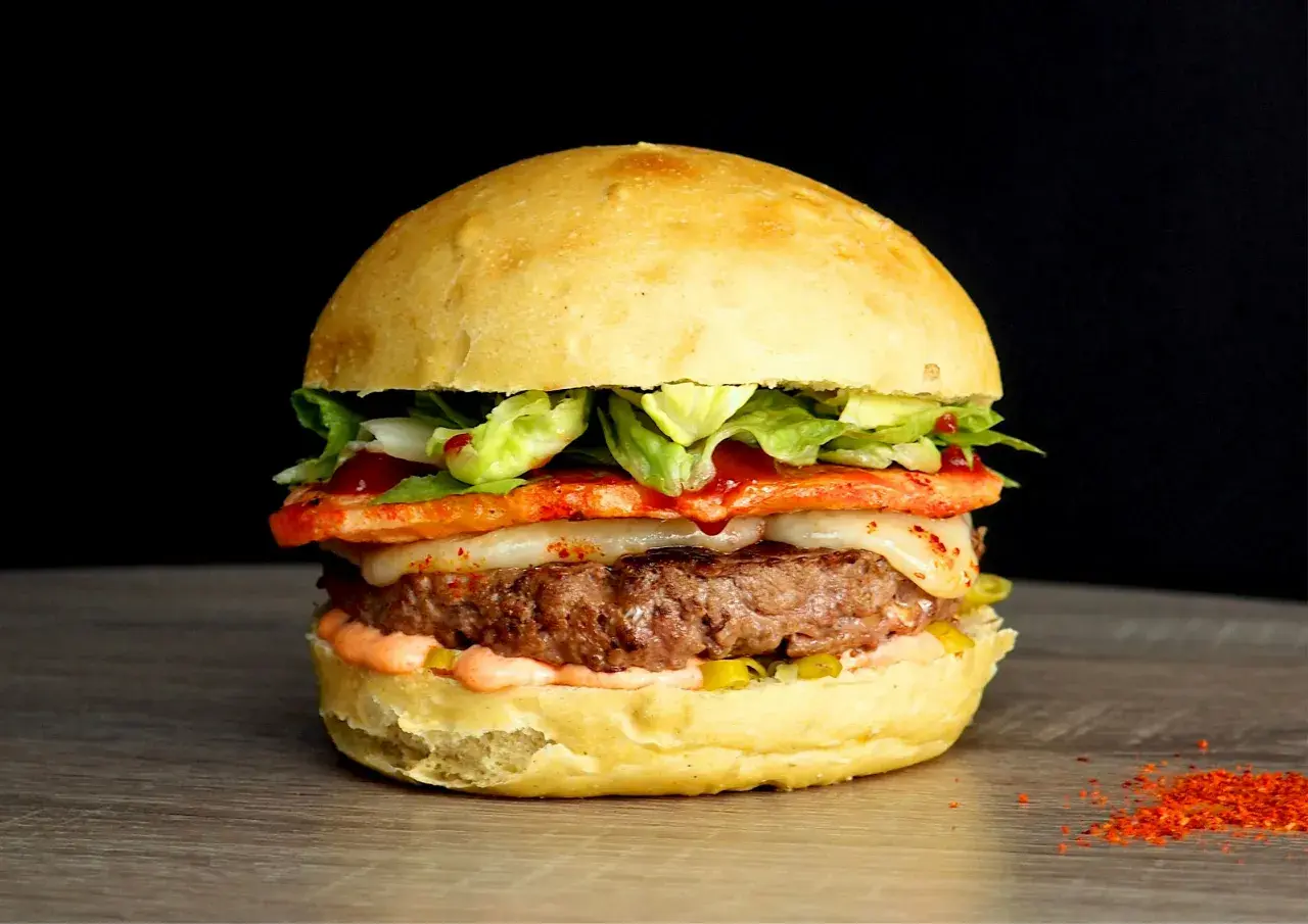 Un généreux burger savoyard avec un steak juteux, fromage fondant, légumes frais et une touche de piment sur un pain brioché.