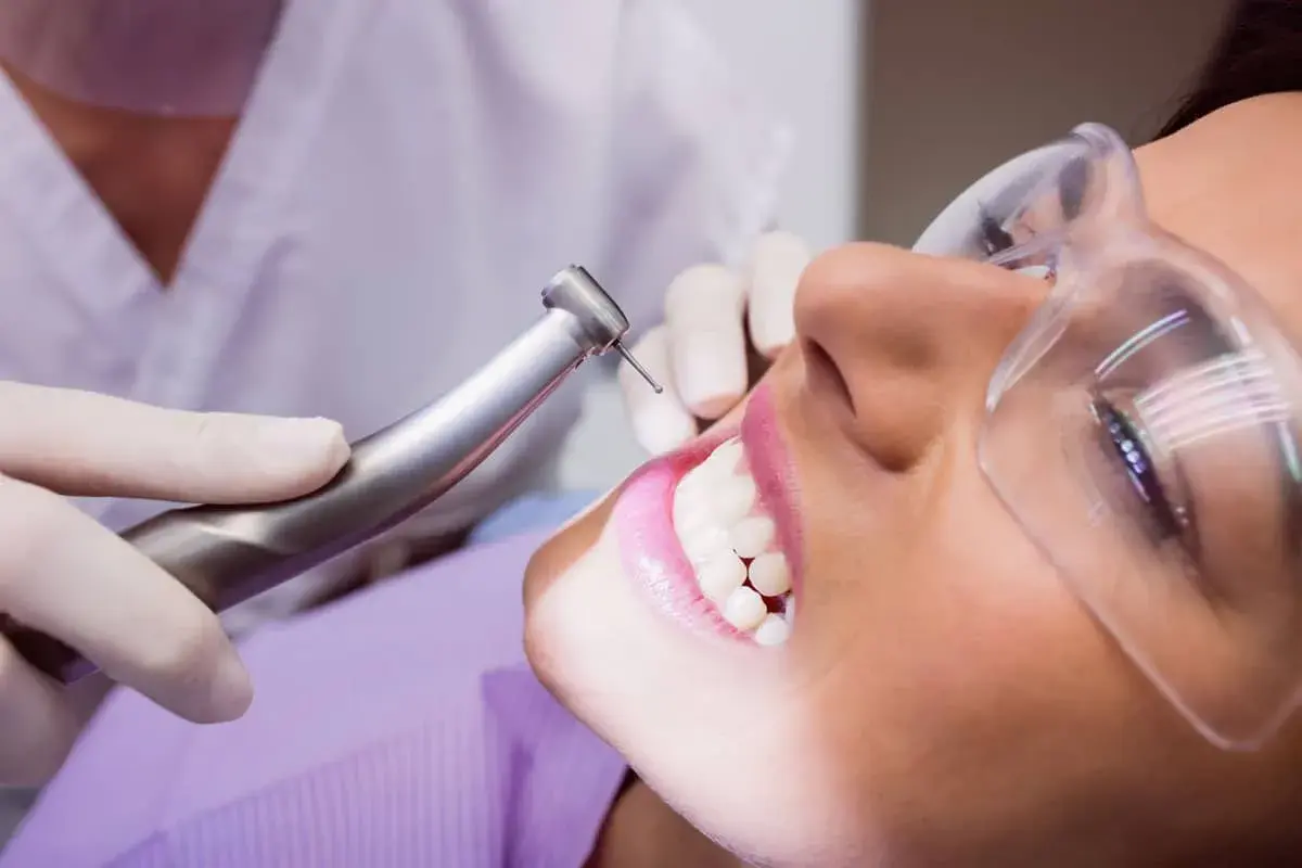 Visita dentistica per rimuovere il tartaro dai denti. La paziente indossa occhiali protettivi mentre il dentista usa uno strumento rotante.