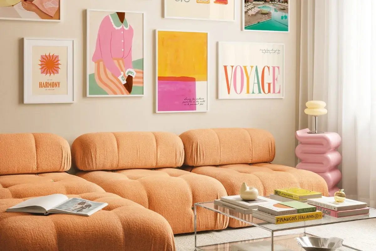 Ein orangefarbenes Sofa mit bunten Bildern an der Wand. Welche Farbe passt zu Orange? Pink und Gelb harmonieren hier perfekt.