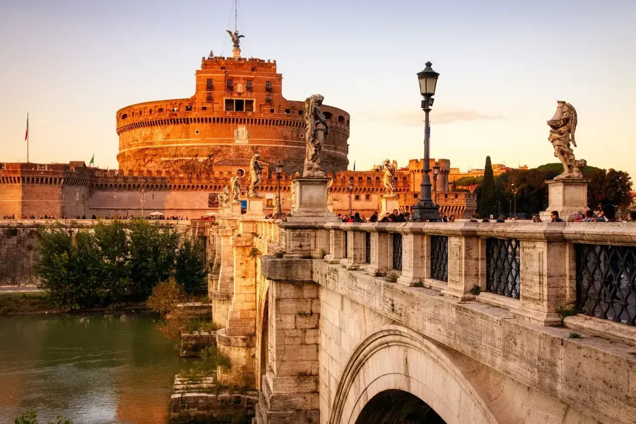 Le pont Saint-Ange à Rome, orné de statues d'anges, mène au château Saint-Ange au coucher du soleil.