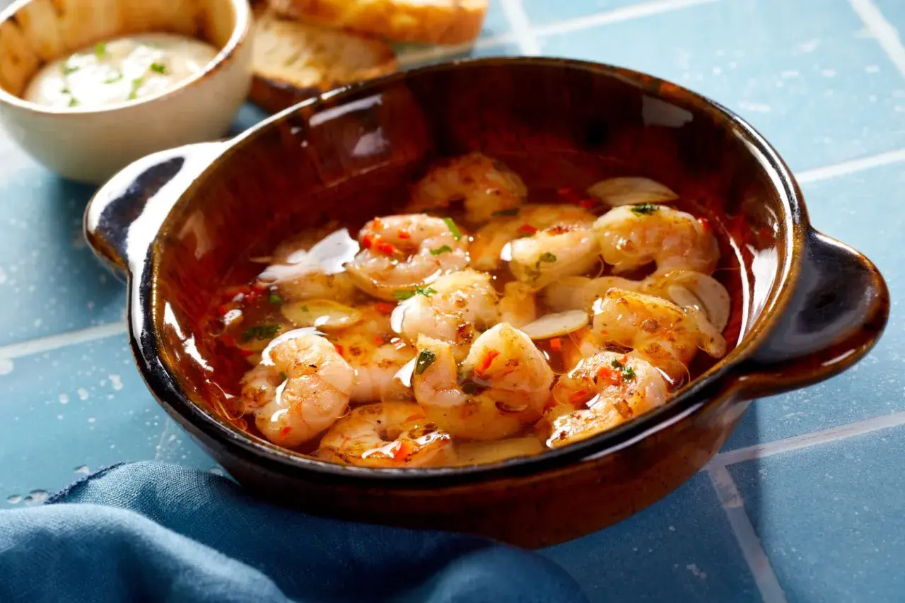 En skål med saftiga gambas pil pil, simmande i vitlök och chiliolja, redo att avnjutas med rostat bröd.