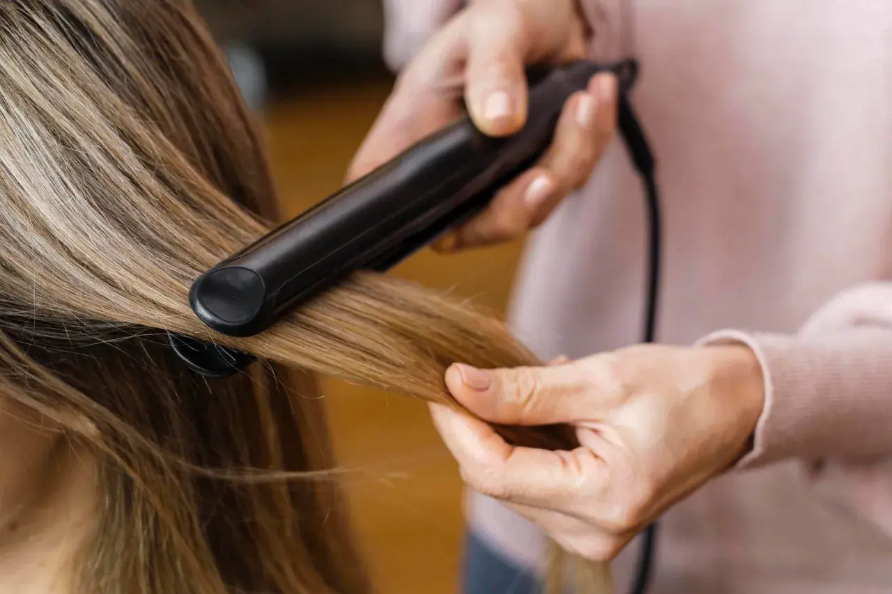 Hårstylist rätar ut frissigt hår uppe på huvudet med ett plattång.