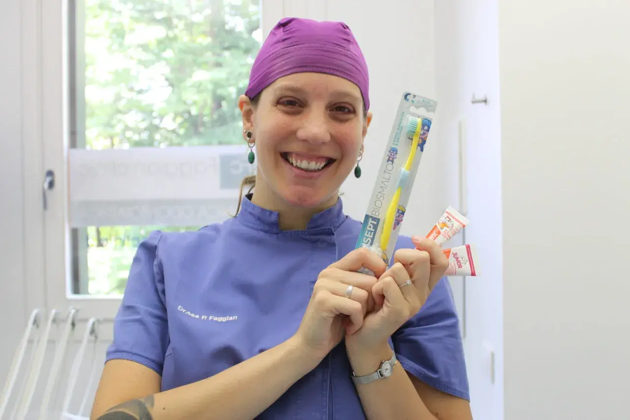 Sorriso di un dentista che mostra spazzolino e dentifrici per la pulizia dei denti bambini.