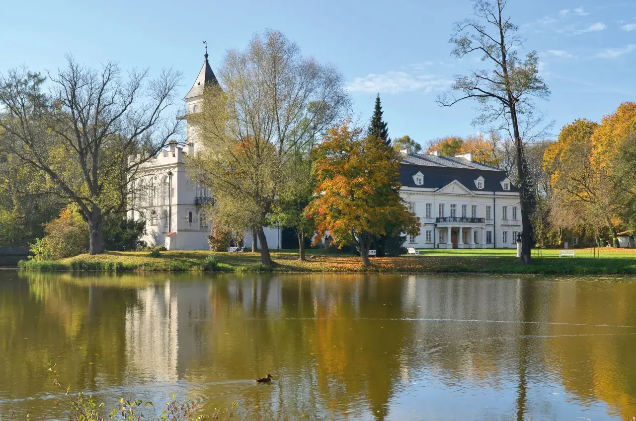 Pałac w Bolimowskim Parku Krajobrazowym odbija się w stawie, otoczony jesiennymi drzewami.