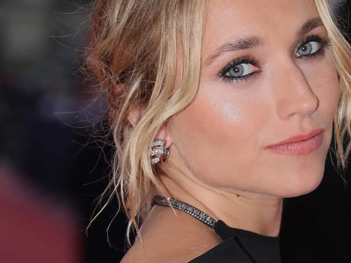Maquillage yeux bleus d'une blonde, avec des boucles d'oreilles scintillantes et un collier discret.
